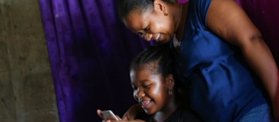 Foto de una madre e hija sonriendo mientras observan un celular