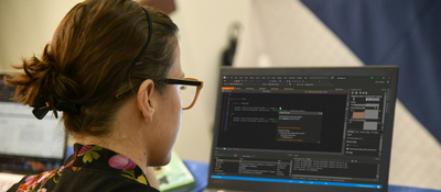 Foto de una mujer con anteojos de espaldas observando un computador