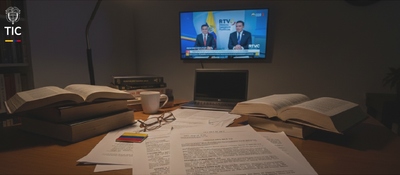 Foto de un escritorio con documentos y al fondo un televisor