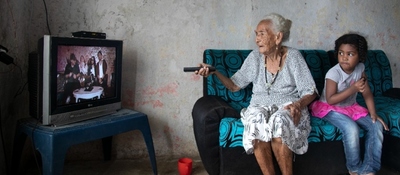 Foto de un adulto mayor y una niña viendo TV