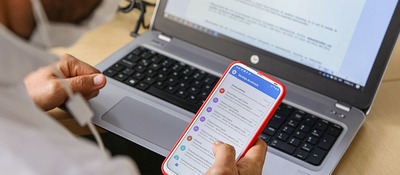 Foto de usuario usando un portatil y consultando su móvil