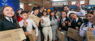 Estudiantes sonríen en evento TIC, sostienen cajas de equipos y hacen señal de paz junto a organizadores en un coliseo escolar