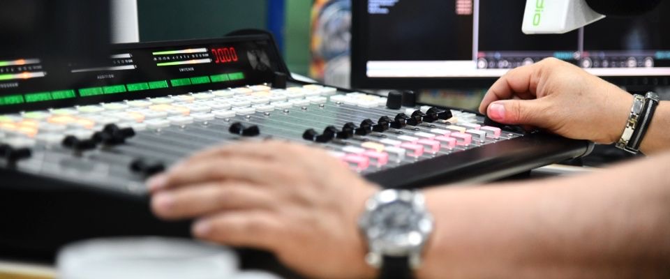 Operador ajusta consola de mezcla en cabina de radio frente a monitores, durante control técnico de transmisión en emisora