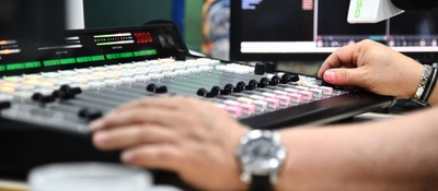 Operador ajusta consola de mezcla en cabina de radio frente a monitores, durante control técnico de transmisión en emisora