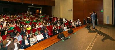 Conferencista interviene desde el escenario ante auditorio lleno durante evento institucional con participación de ciudadanos y expertos