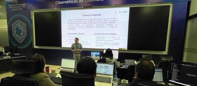 Experto expone sobre ciberseguridad ante un grupo de asistentes con portátiles, frente a una pantalla con información sobre contexto regional y protección digital
