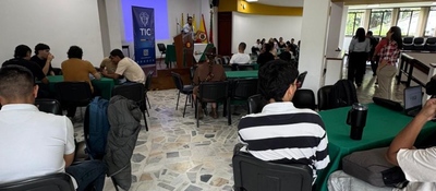 En un salón de Pereira, personas sentadas en mesas escuchan a un expositor frente a un podio del TIC, en encuentro sobre Educación Digital