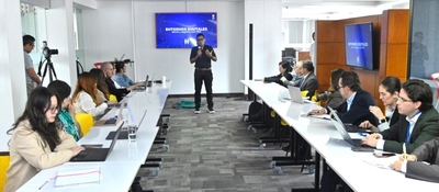 Sala de reuniones: un expositor presenta “Entornos Digitales” frente a una pantalla mientras funcionarios escuchan y trabajan con portátiles en mesas largas.