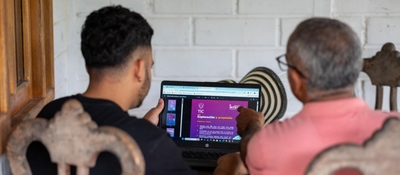 Dos personas observan un computador portátil que muestra información del Ministerio TIC, revisando contenidos digitales sobre conectividad y tecnología