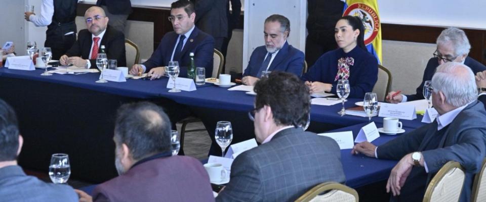 Funcionarios y técnicos se reúnen en mesa formal con bandera de Colombia, revisando documentos sobre auditoría del software electoral