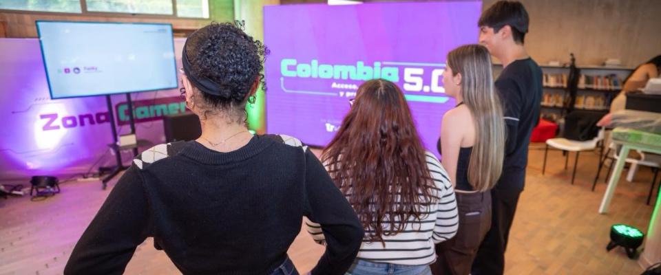 Jóvenes observan una pantalla en zona interactiva de Colombia 5.0, con luces de colores y ambiente tecnológico en Manizales