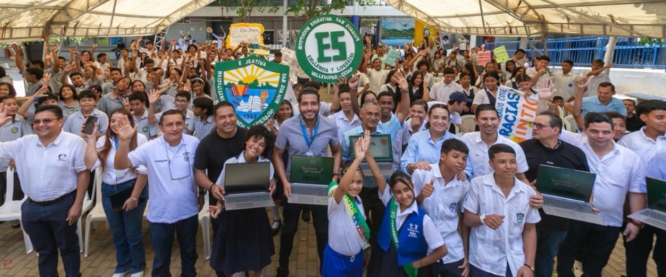 Grupo grande posa con laptops nuevas en colegio; ambiente festivo por llegada de computadores y conectividad a zonas rurales e indígenas.