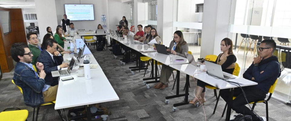 Personas en sala moderna trabajan con portátiles en mesas largas. Avanza reglamentación de Entornos Digitales Sanos con apoyo pedagógico.