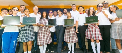 Grupo de estudiantes con uniformes escolares sostienen portátiles, acompañados de adultos, en un evento de entrega tecnológica en Atlántico