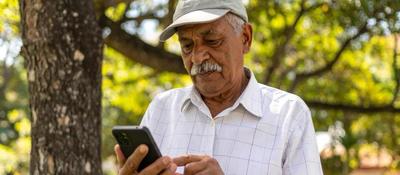 Hombre mayor usa celular bajo un árbol. Representa acceso a telecomunicaciones y oportunidades para servicios comunitarios en banda 900 MHz.