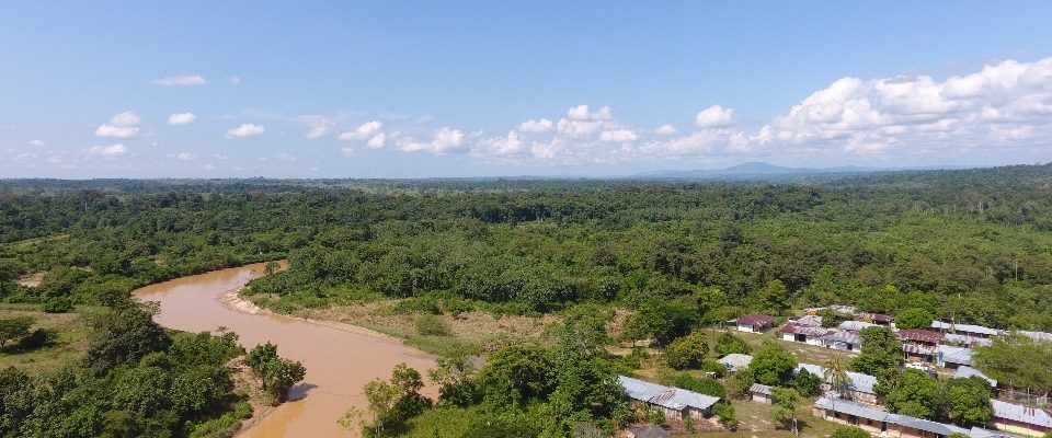 Vista aérea de un río marrón que serpentea entre selva densa; a un lado, un pequeño caserío rural rodeado de verde en el Magdalena Medio.