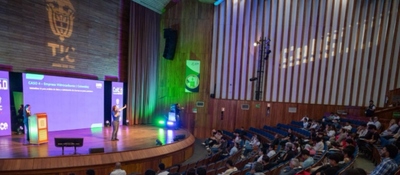 Auditorio amplio con escenario iluminado; ponente expone sobre Colombia 5.0 ante público sentado, con logos TIC y pantallas digitales.
