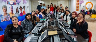 Grupo de mujeres en aula TIC con computadores, sonríen a cámara durante formación técnica impulsada por MinTIC e IPES.