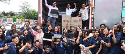 Grupo de estudiantes y adultos celebra frente a un camión abierto con cajas y portátiles, símbolo de entrega tecnológica para educación.