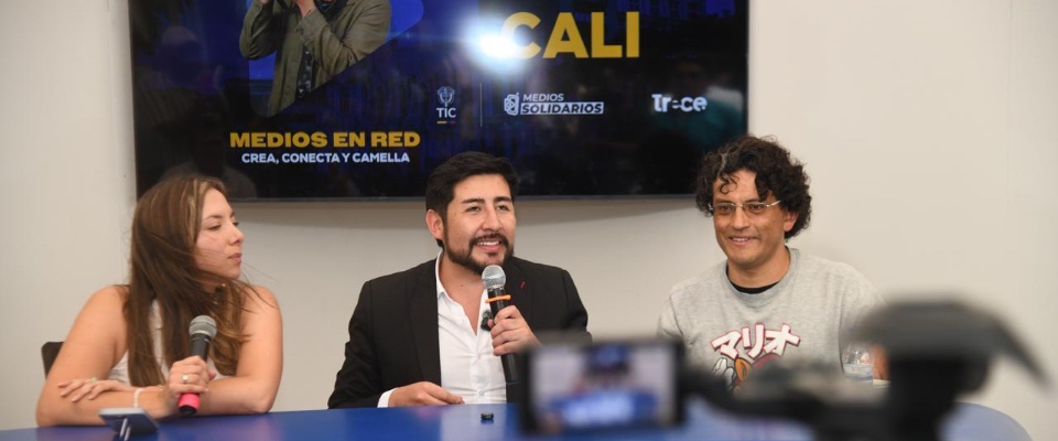 Tres panelistas en mesa hablan con micrófonos; pantalla atrás dice Cali y Medios en Red, sobre impulso a innovación y medios comunitarios.