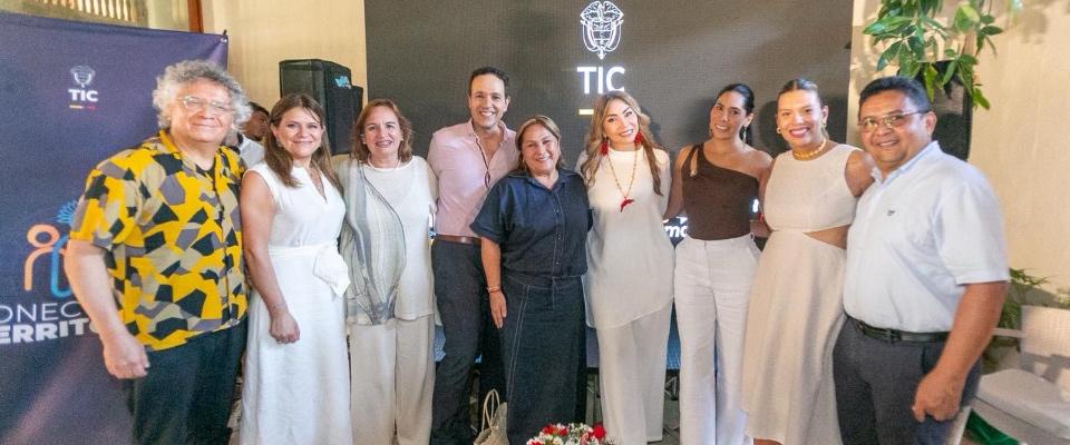 Grupo de nueve adultos posa sonriente frente a fondo con logo TIC; evento anuncia convocatorias audiovisuales Historias del Cambio.