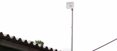 Antena de telecomunicaciones elevada sobre un poste junto a un techo, simboliza conectividad y expansión de redes en zonas apartadas.