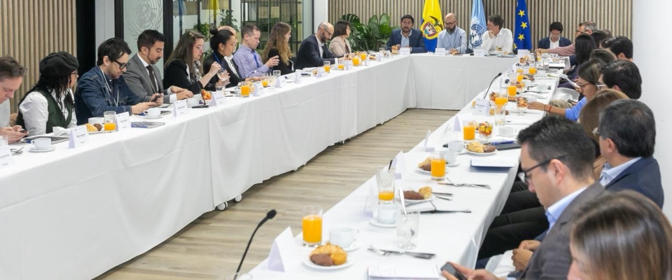 Personas en mesa larga de reunión con jugo y café, dialogan sobre estrategia conjunta para impulsar la transformación digital inclusiva en Colombia