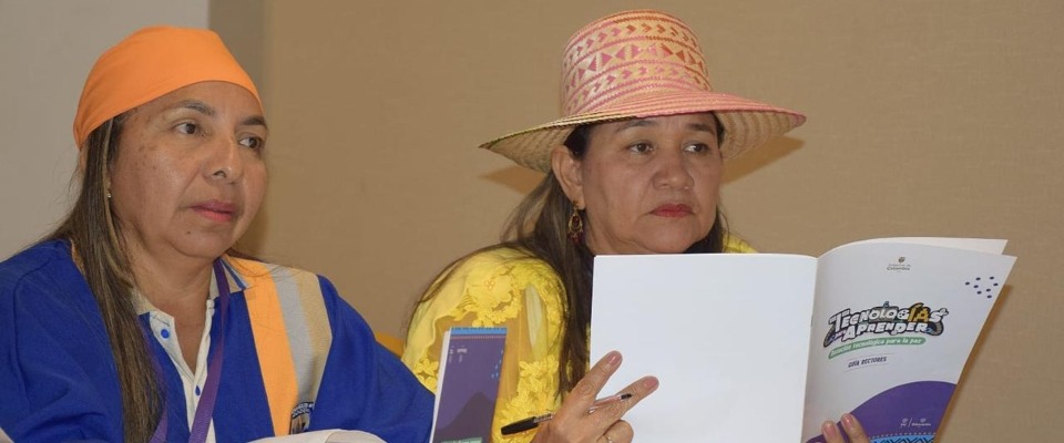 Dos mujeres, una con chaleco y otra con sombrero, revisan un documento en reunión sobre formación docente en inteligencia artificial.