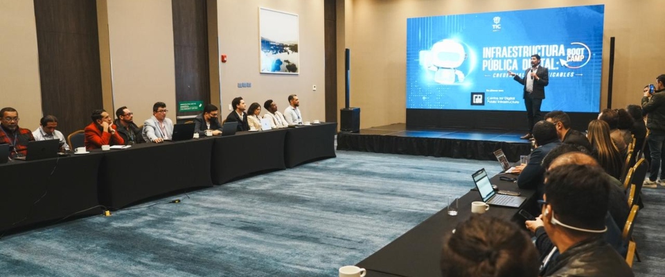 Salón de conferencia: asistentes con portátiles escuchan a un expositor frente a pantalla sobre trámites digitales del Estado.