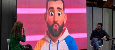 Panel sobre medios públicos y conectividad con dos personas en escenario y personaje animado proyectado en pantalla gigante.