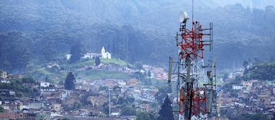Antena de telecomunicaciones domina un barrio urbano rodeado de montañas y bosque, símbolo de conectividad y uso del espectro