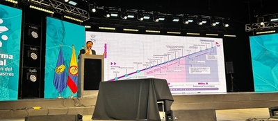 Funcionario presenta sistema digital de gestión del riesgo en escenario con pantallas y banderas institucionales