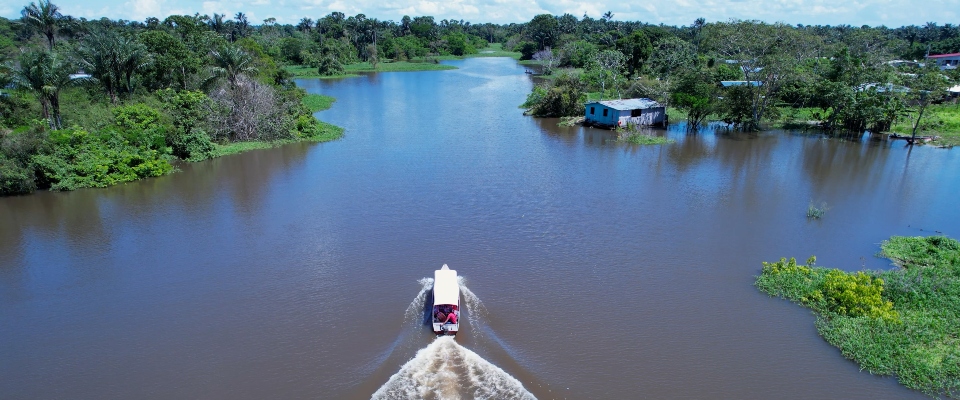 Vista aérea de un río amazónico con una lancha avanzando entre casas y selva inundada por crecientes de agua