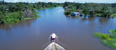 Vista aérea de un río amazónico con una lancha avanzando entre casas y selva inundada por crecientes de agua