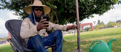 Trabajador rural usa celular mientras descansa en zona verde, reflejando expansión de conectividad en municipios del país