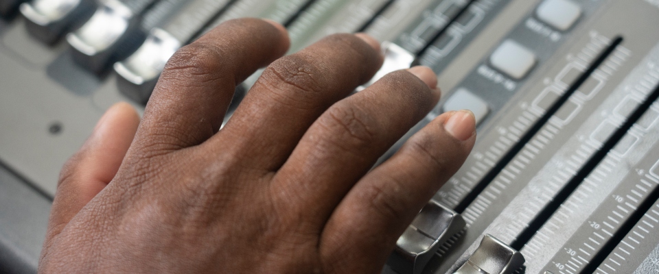 Primer plano de una mano operando una consola de audio. La imagen representa la radiodifusión comunitaria y la comunicación local. Primer plano de una mano operando una consola de audio. La imagen representa la radiodifusión comunitaria y la comunicación local.