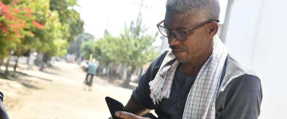 Hombre con gafas consulta su celular en una zona rural. La imagen representa acceso y conectividad para las comunidades Hombre con gafas consulta su celular en una zona rural. La imagen representa acceso y conectividad para las comunidades