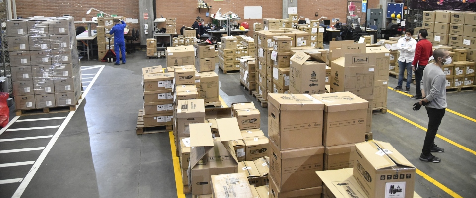 Vista aérea de un centro logístico con estanterías repletas de cajas, montacargas y personal organizando envíos
