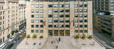 Fachada del edificio del Ministerio TIC en Bogotá, con banderas de Colombia y personas en la plaza frente al ingreso