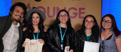 Cinco asistentes sonríen frente al panel de un evento, con acreditaciones y materiales, tras anuncio de nominados a Premios TAL.