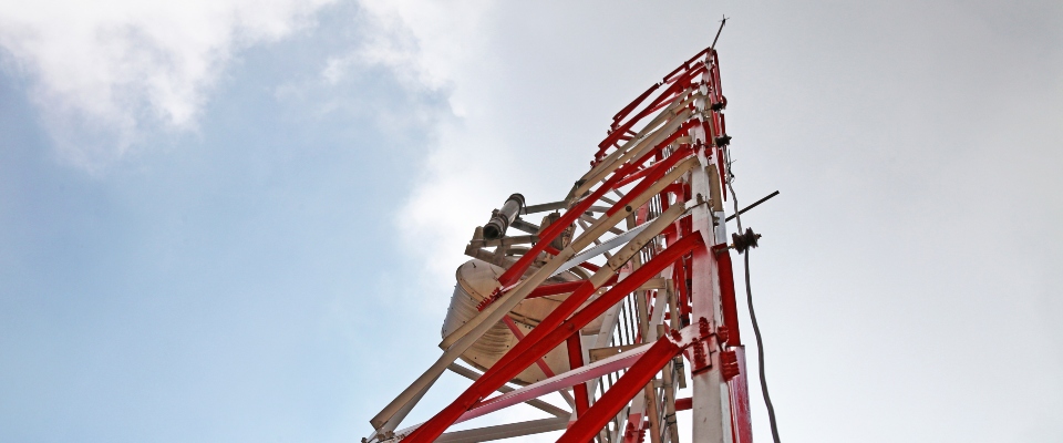 Torre de telecomunicaciones roja y blanca vista desde su base hacia el cielo. Representa la conectividad y el uso del espectro.