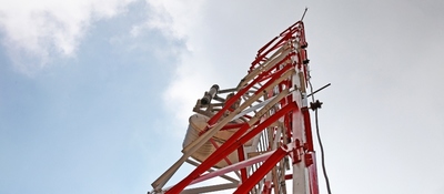 Torre de telecomunicaciones roja y blanca vista desde su base hacia el cielo. Representa la conectividad y el uso del espectro.