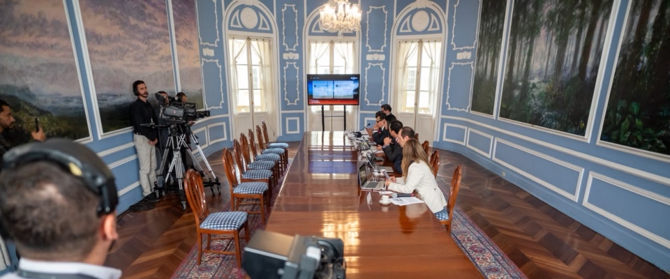 Sala de reuniones con mesa larga, funcionarios y periodistas. Al fondo, una pantalla durante una rueda de prensa oficial. Sala de reuniones con mesa larga, funcionarios y periodistas. Al fondo, una pantalla durante una rueda de prensa oficial.
