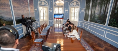 Sala de reuniones con mesa larga, funcionarios y periodistas. Al fondo, una pantalla durante una rueda de prensa oficial.