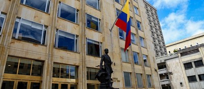 Edificio del mMinisterio TIC con dos banderas de Colombia y una estatua al frente, bajo un cielo azul con nubes
