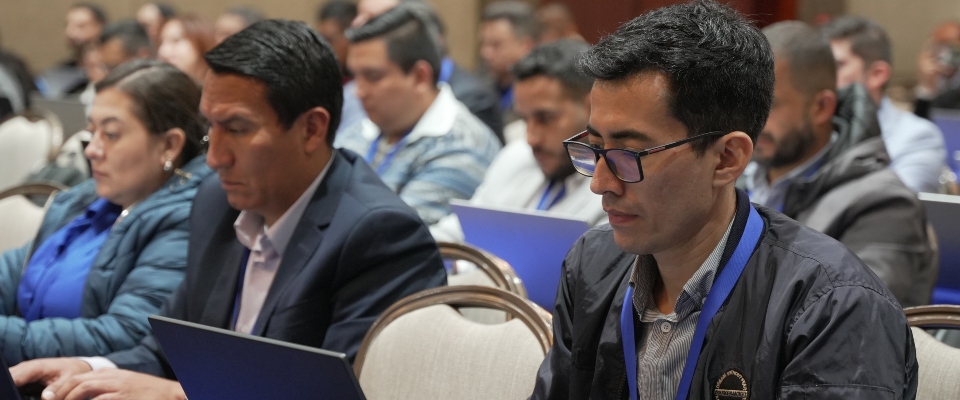 Personas sentadas con portátiles en una sala; al frente, un hombre con gafas mira su pantalla y otros observan sus equipos