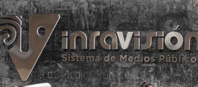 Logotipo de RTVC en tonos gris y beige sobre una pared oscura