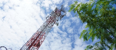 Torre metálica roja y blanca con antenas, bajo un cielo nublado; un árbol verde ocupa el lado derecho