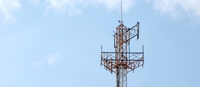 Antena de telecomunicaciones metálica con múltiples paneles y cables, sobre un cielo azul con nubes.