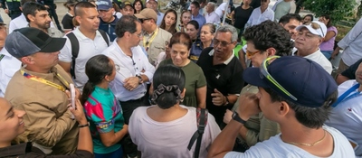 Grupo numeroso de personas rodea a varias mujeres en un espacio exterior; algunas conversan y otras observan